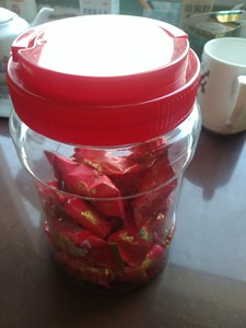 出一罐喜糖，罐子是透明的塑料材质，红色的盖子和包装，里面装满